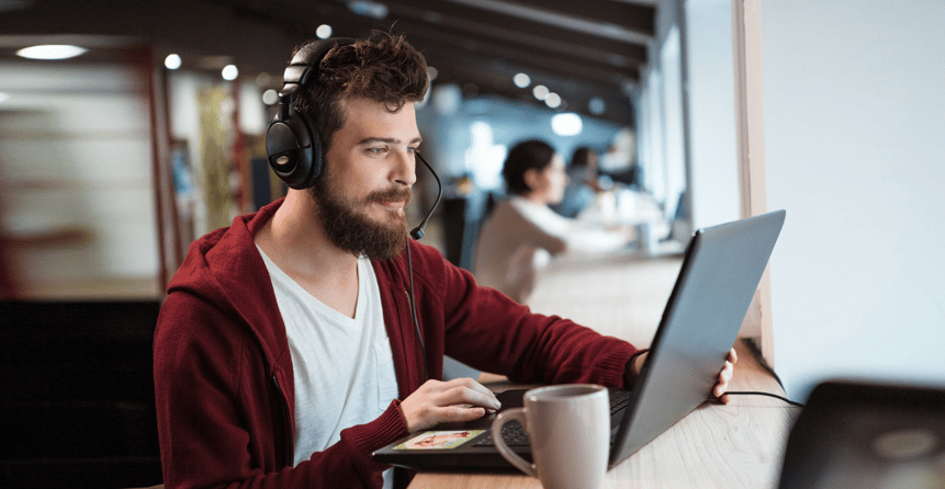 Concentrated handsome male with beard using headset and laptop.png