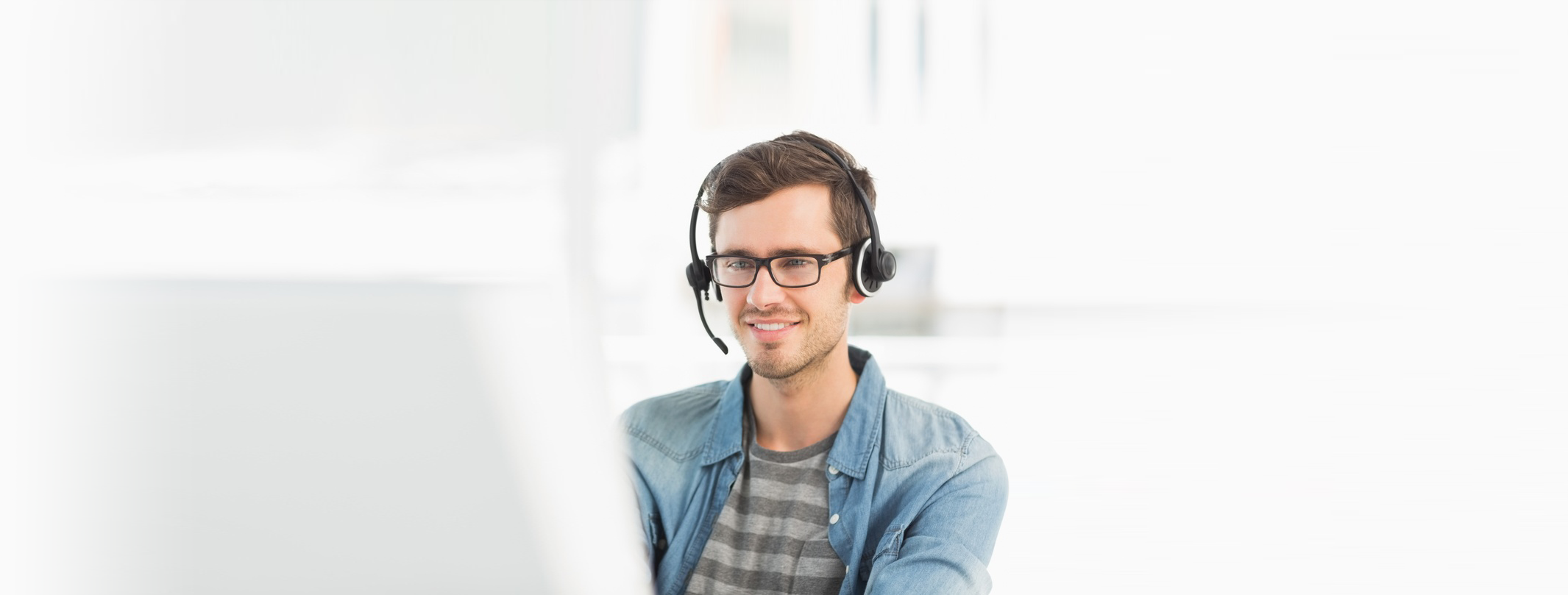 Smiling casual young man with headset using computer in a bright officev3